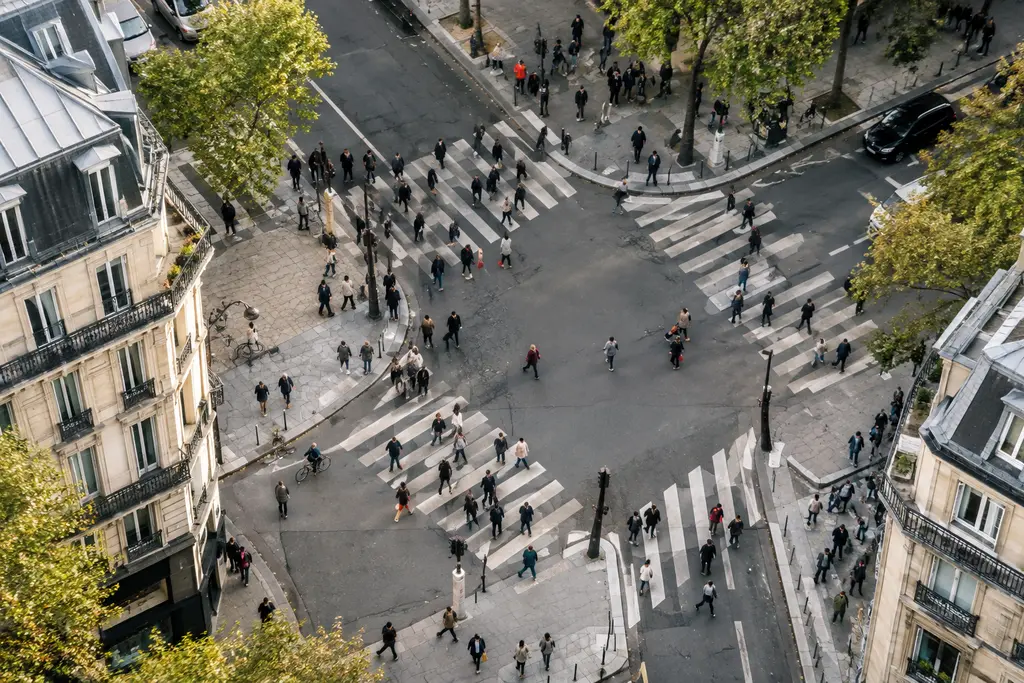 Des flux de piétons convergent sur les passages d’un carrefour parisien vu d’en haut.