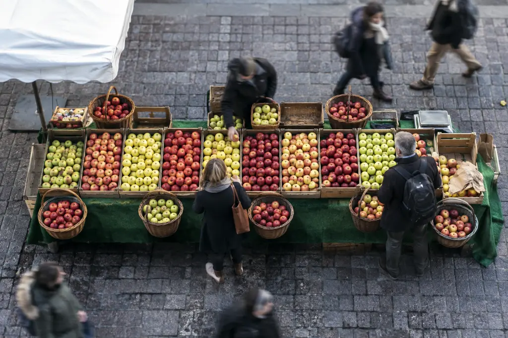 Des pommes rangées sur un étal de marché, avec vendeurs et acheteurs en arrière-plan.